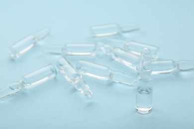 Glass ampoules with liquid on light blue background, closeup