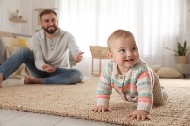 Photo of Happy young father watching his cute baby crawl on floor at home