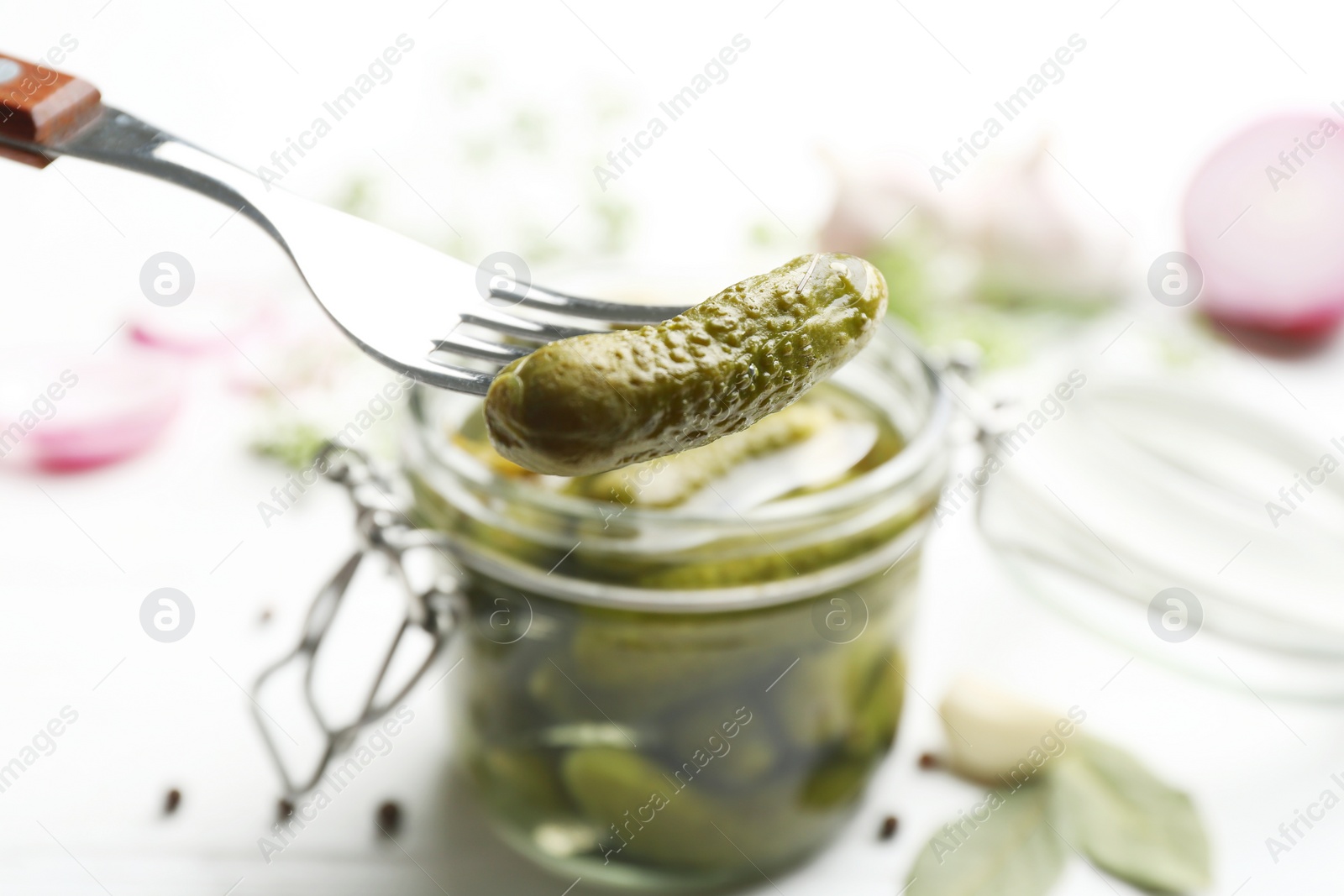 Photo of Fork with tasty pickled cucumber near glass jar, closeup