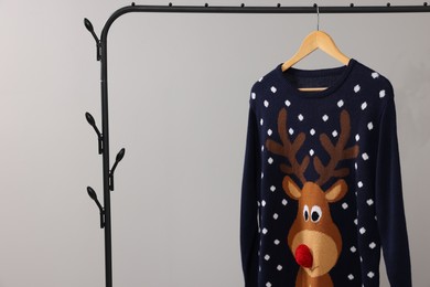 Rack with Christmas sweater on light background