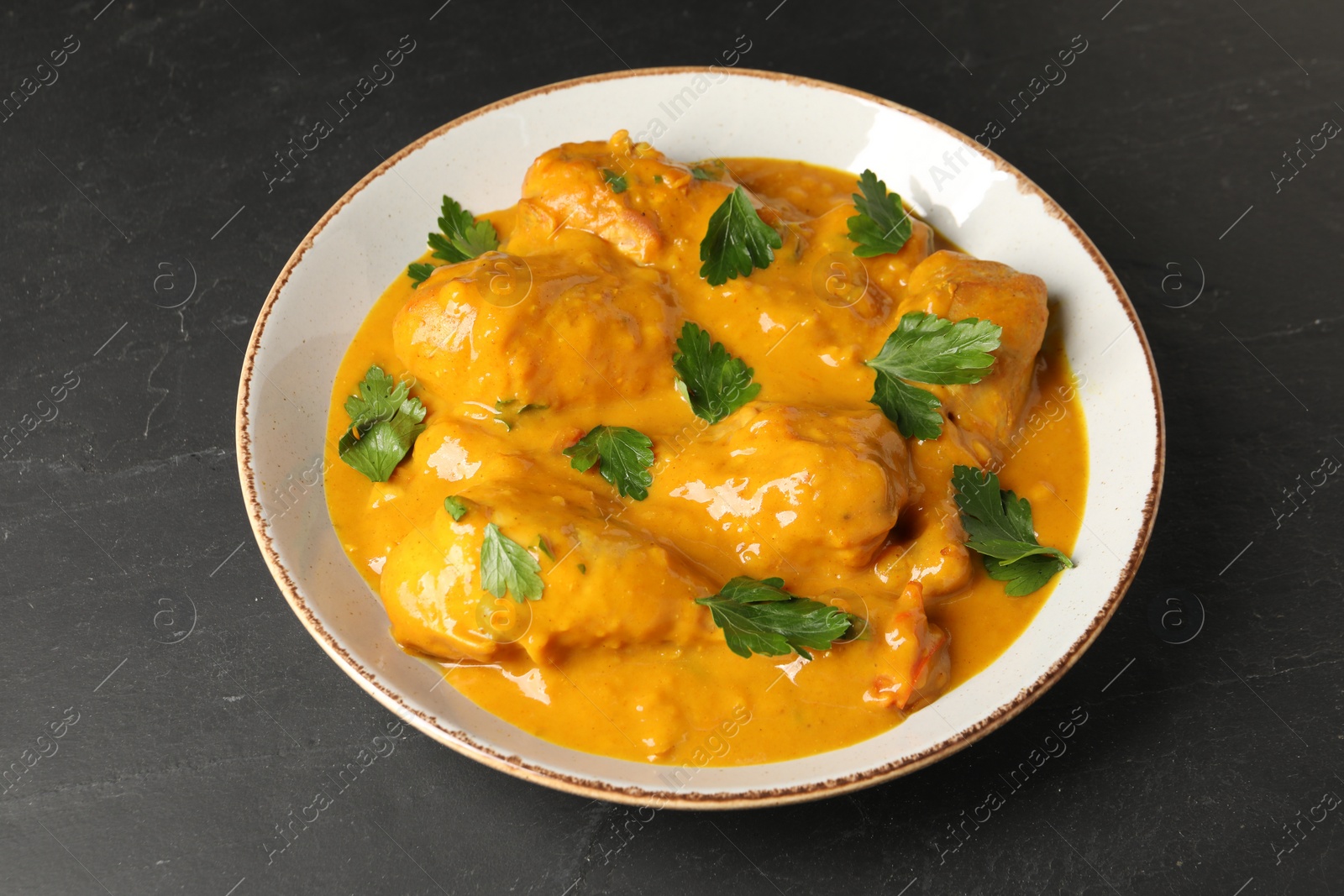 Photo of Tasty chicken curry with parsley on black textured table