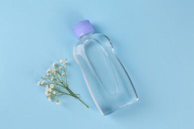 Photo of Bottle with baby oil and gypsophila on light blue background, flat lay. Space for text