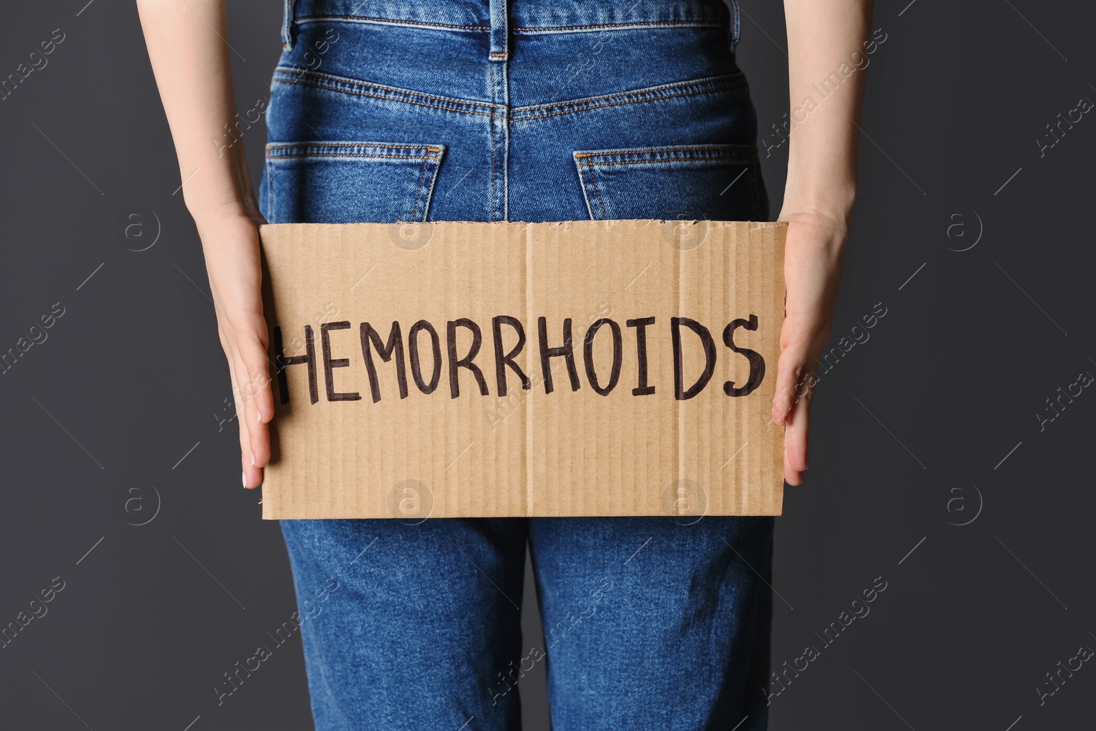 Photo of Woman holding carton sign with word HEMORRHOIDS on black background, closeup