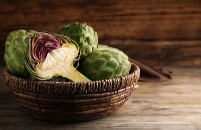 Photo of Cut and whole fresh raw artichokes in basket on wooden table