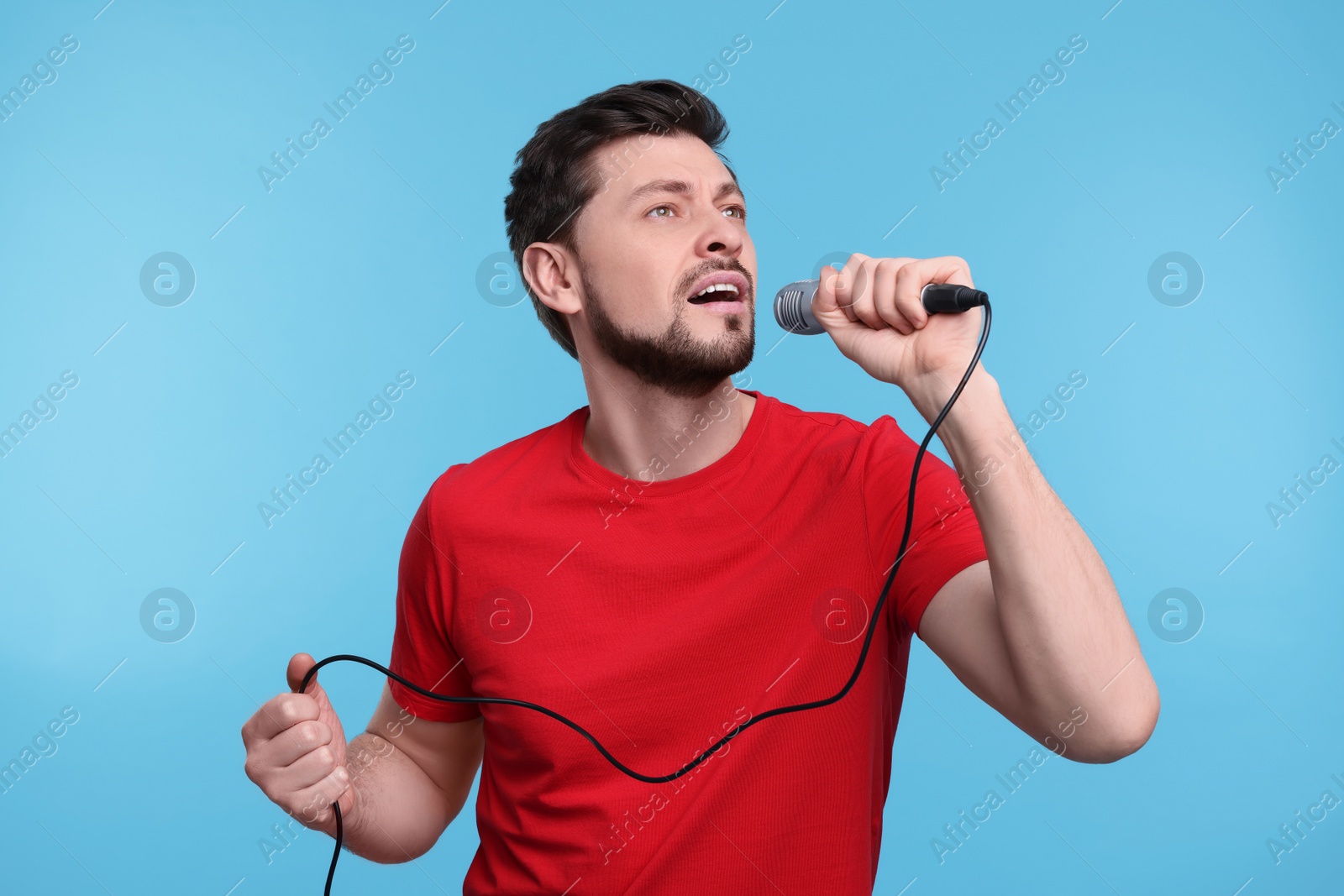 Photo of Handsome man with microphone singing on light blue background