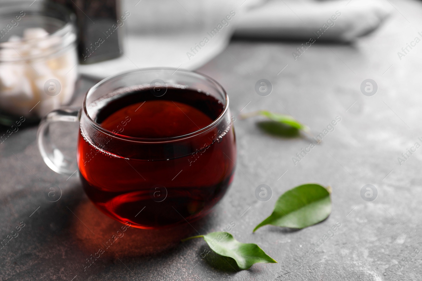 Photo of Tasty hot tea in cup and leaves on grey table, closeup. Space for text