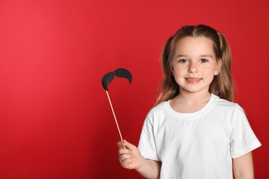 Photo of Funny little girl with fake mustache on red background, space for text