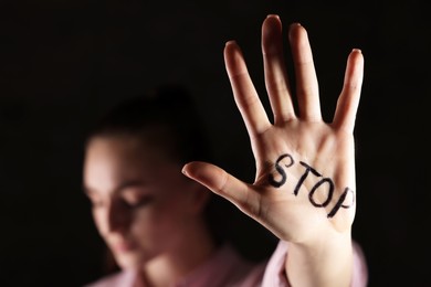 Photo of Woman with word Stop written on hand against dark background, closeup. Domestic violence concept