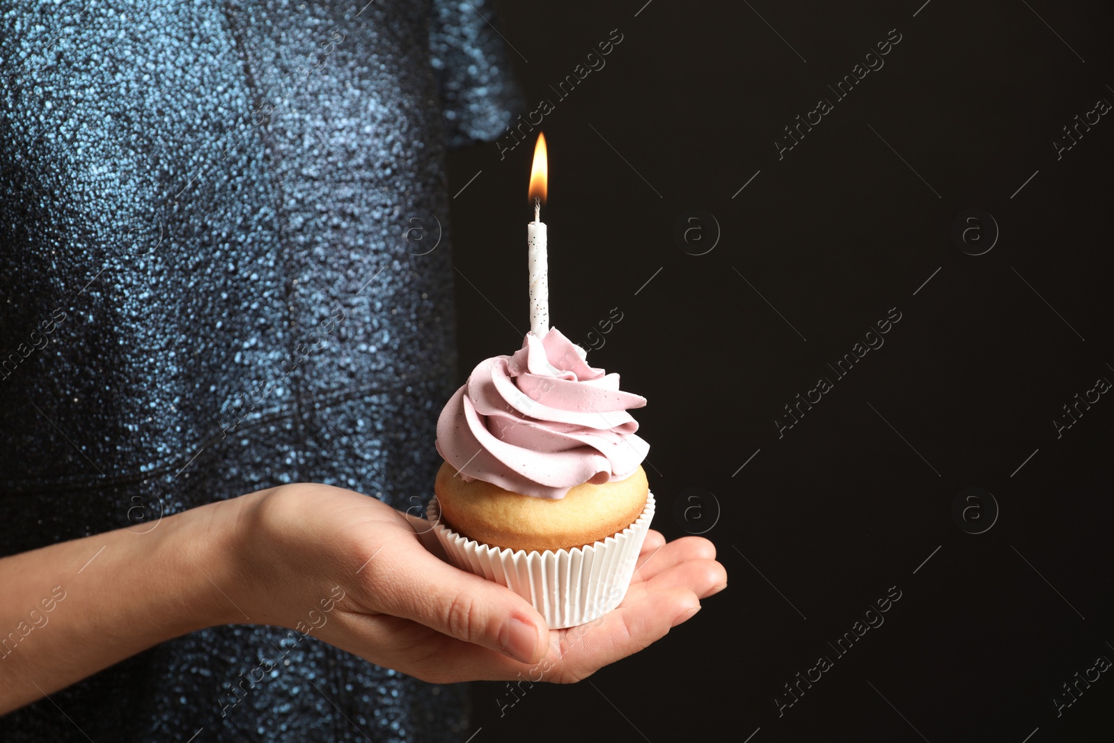 Photo of Woman holding delicious birthday cupcake with burning candle on black background, closeup