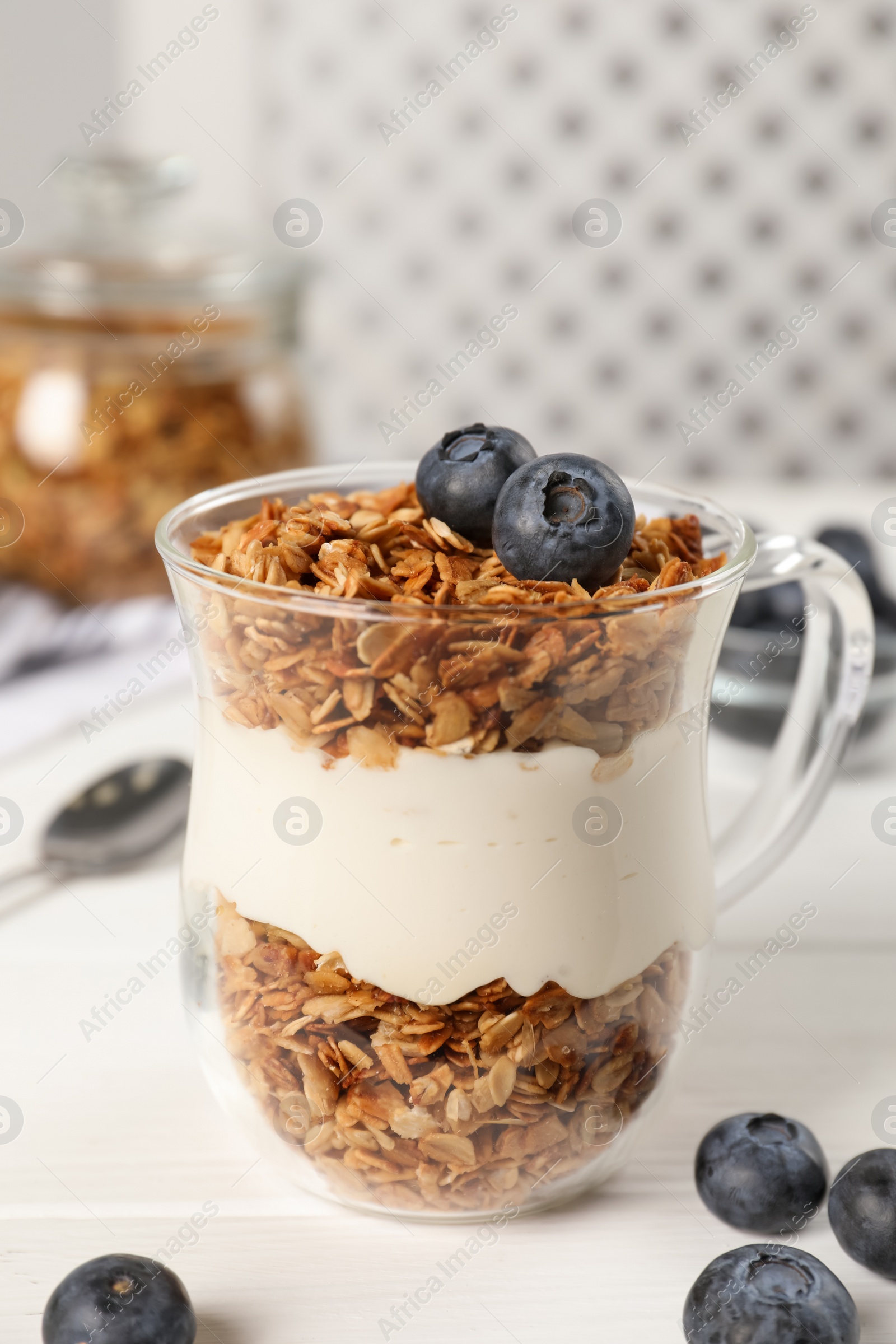 Photo of Tasty yogurt with muesli and blueberries in cup served on white wooden table