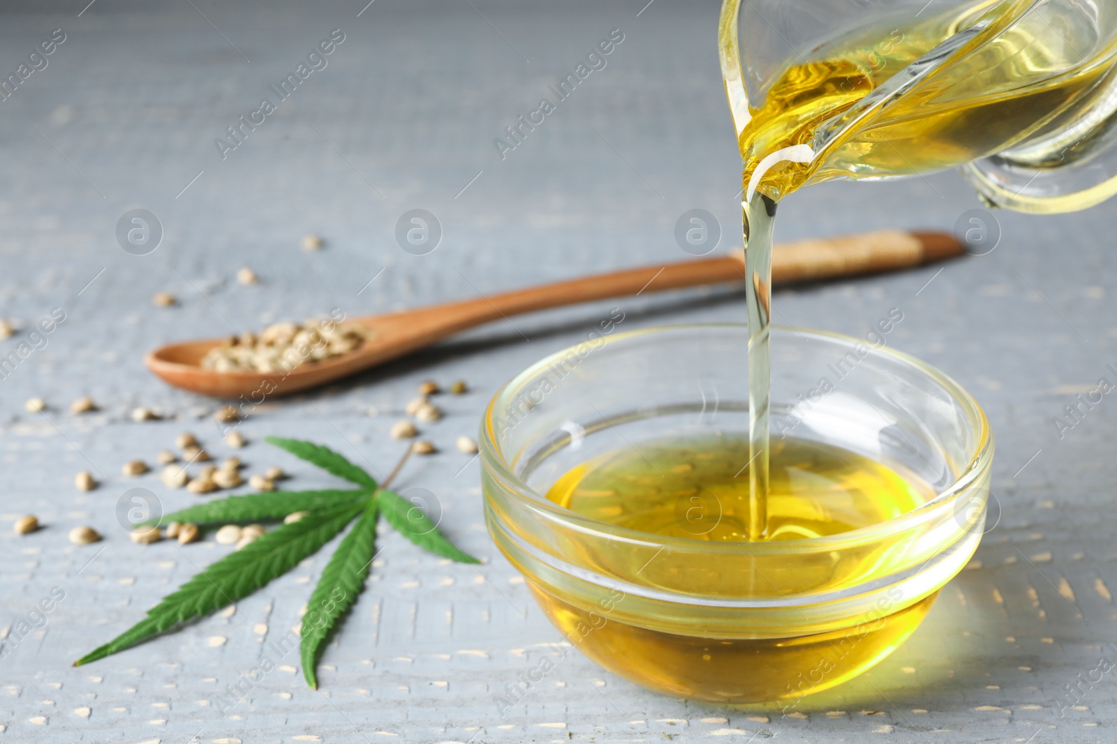 Photo of Hemp oil pouring from sauce boat into bowl on table