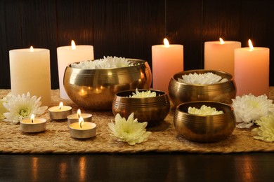 Photo of Tibetan singing bowls with beautiful flowers and burning candles on wooden table