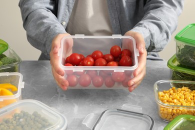 Photo of Man holding plastic container with fresh cherry tomatoes at light grey table in kitchen, closeup. Food storage