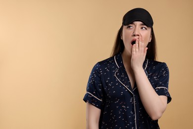 Tired young woman with sleep mask yawning on beige background, space for text. Insomnia problem