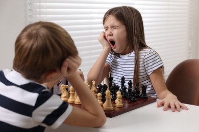 Cute children playing chess at table in room