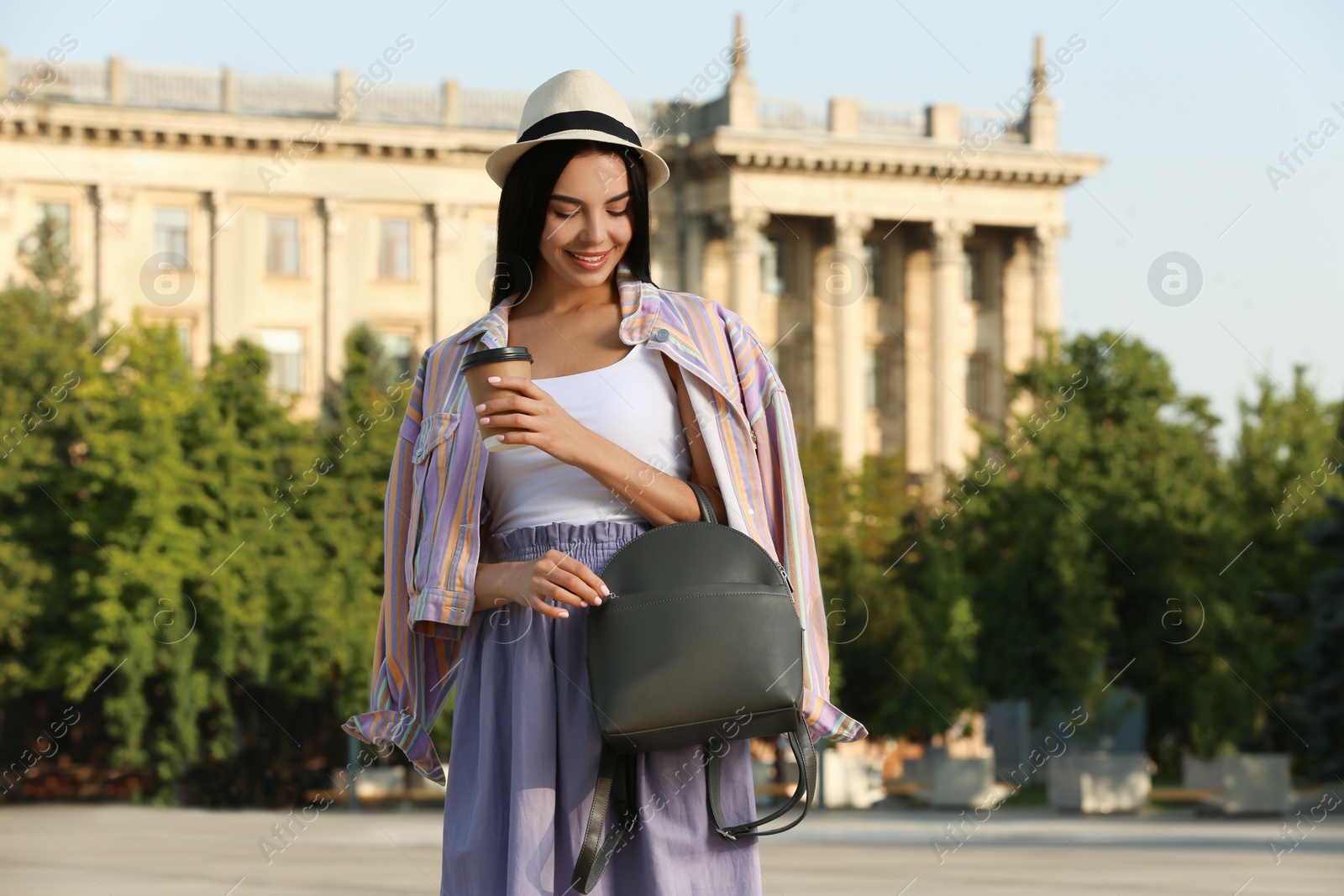 Photo of Beautiful young woman with stylish backpack and coffee on city street