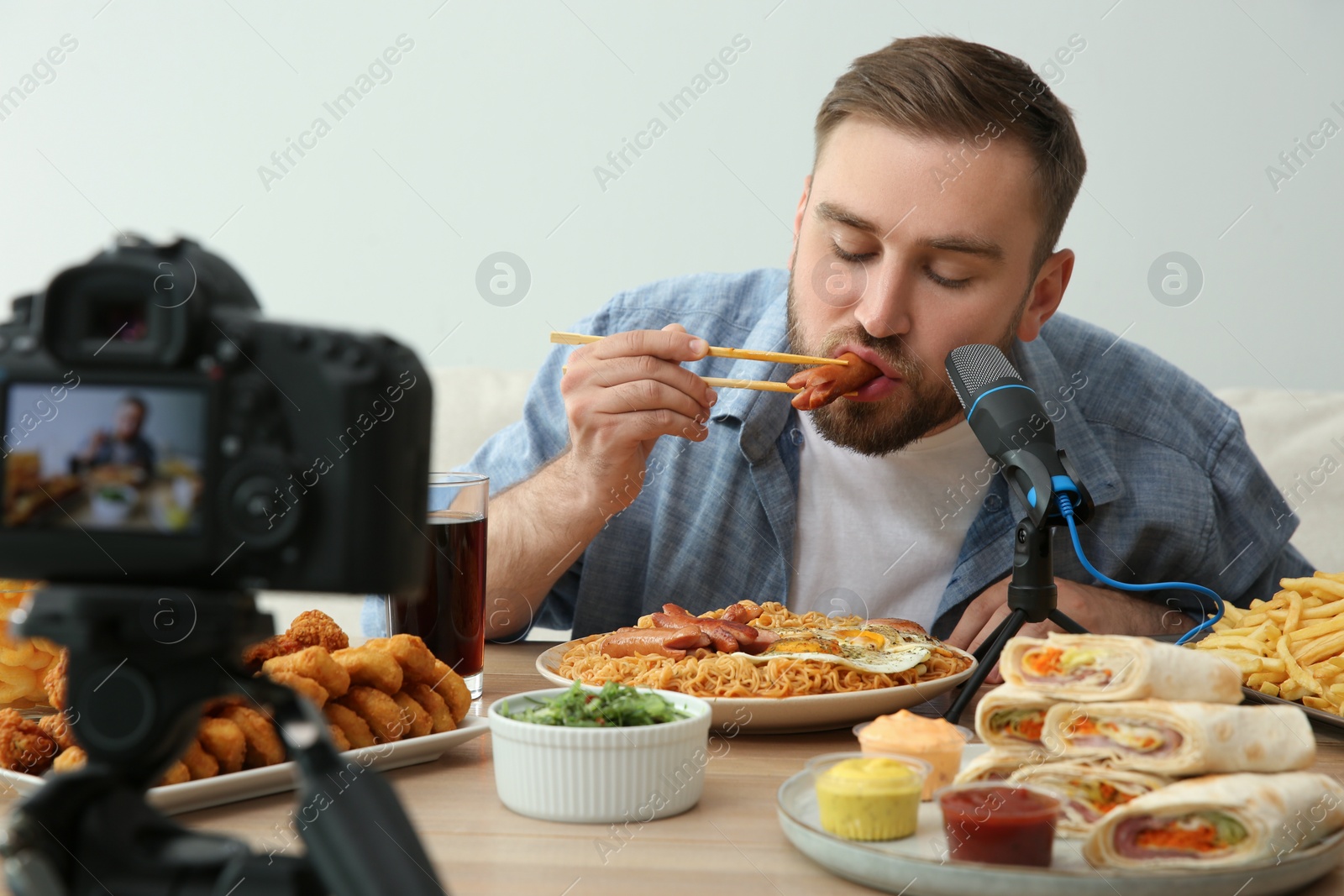 Photo of Food blogger recording eating show on camera against light background. Mukbang vlog