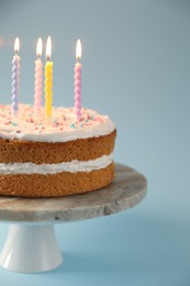 Photo of Tasty cake with colorful candles on light blue background, closeup