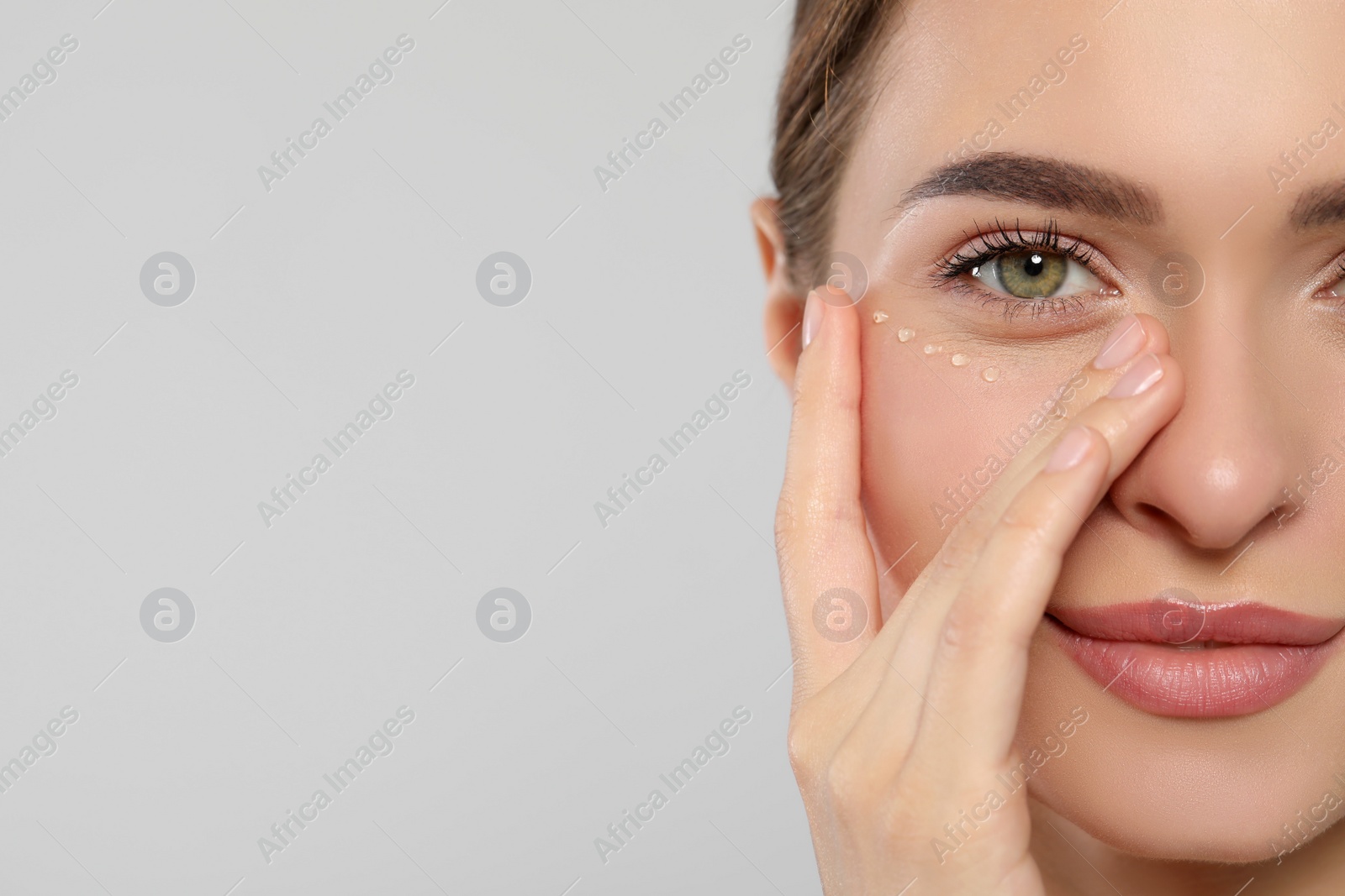 Photo of Young woman with cream around eye on white background, closeup. Space for text