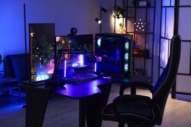 Photo of Playing video games. Stylish room interior with modern computer and gaming chair in neon lights