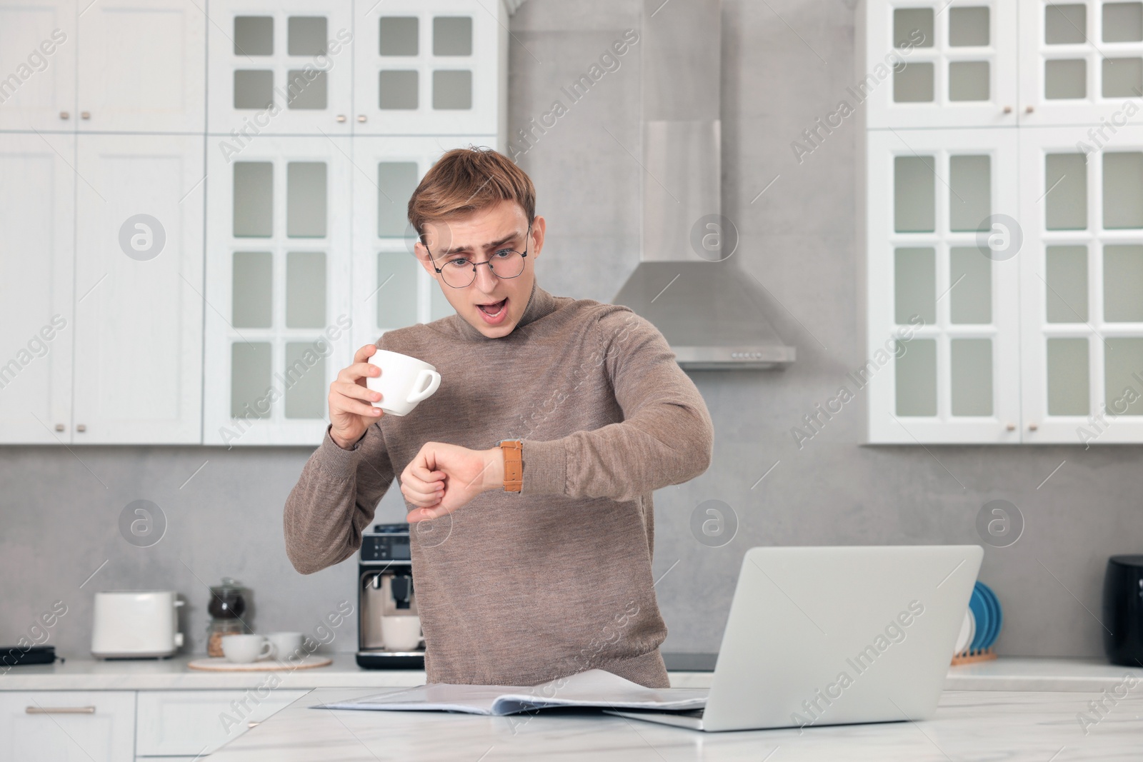 Photo of Emotional young man checking time while drinking coffee in kitchen. Being late