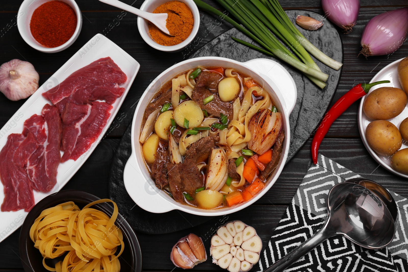 Photo of Pot of delicious vegetable soup with meat, noodles and ingredients on black wooden table, flat lay