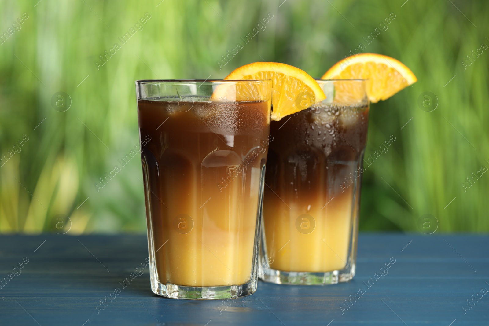 Photo of Tasty refreshing drink with coffee and orange juice on blue wooden table against blurred background