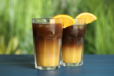 Tasty refreshing drink with coffee and orange juice on blue wooden table against blurred background