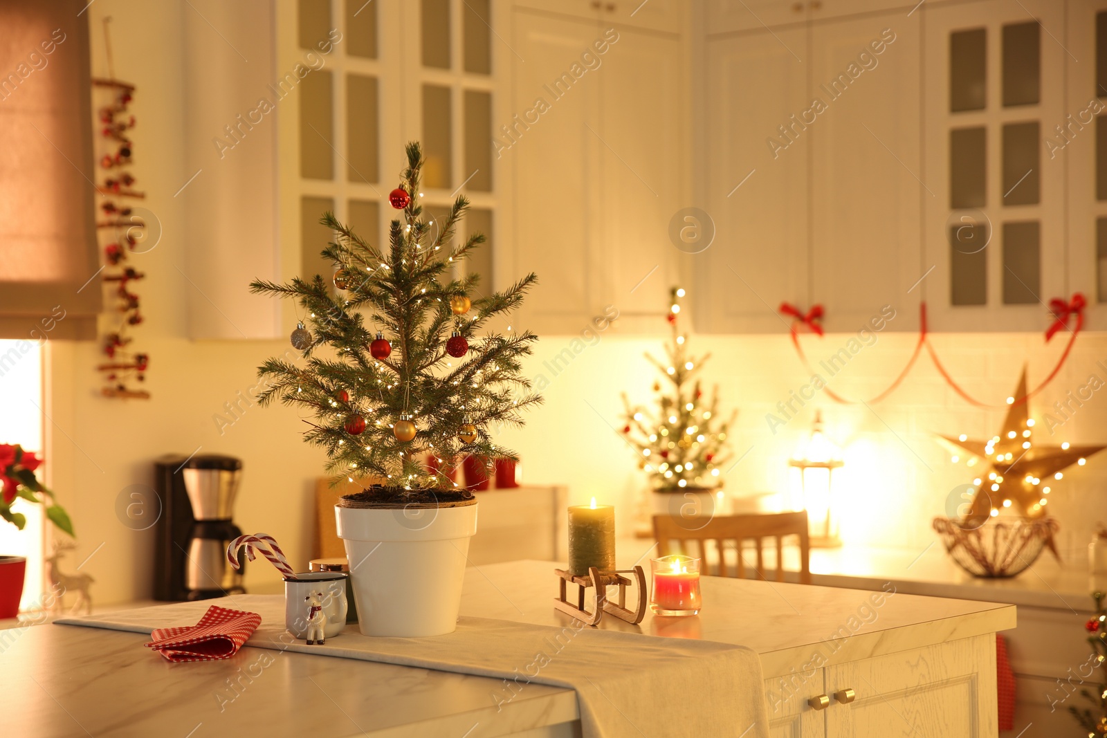 Photo of Small Christmas tree decorated with baubles and festive lights in kitchen. Space for text