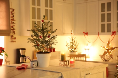 Small Christmas tree decorated with baubles and festive lights in kitchen. Space for text