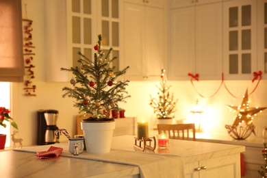 Photo of Small Christmas tree decorated with baubles and festive lights in kitchen. Space for text