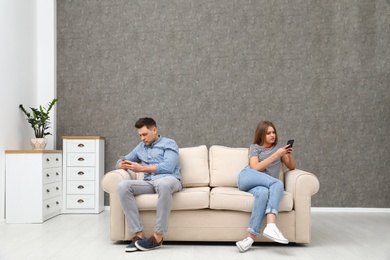 Photo of Couple engaged in smartphones while spending time together at home. Loneliness concept