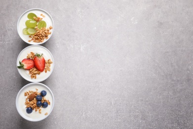 Photo of Bowls with yogurt, granola and different fruits on gray background, top view