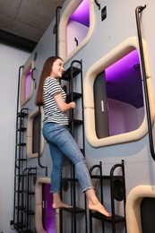 Photo of Happy young woman climbing up ladder to capsule in pod hostel