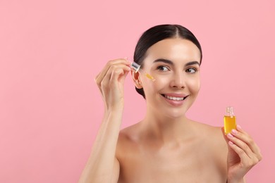 Photo of Beautiful young woman applying serum onto her face on pink background. Space for text
