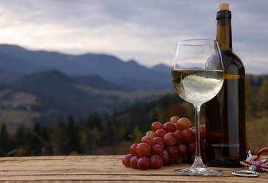 Photo of Tasty wine and fresh grapes on wooden table against mountain landscape. Space for text