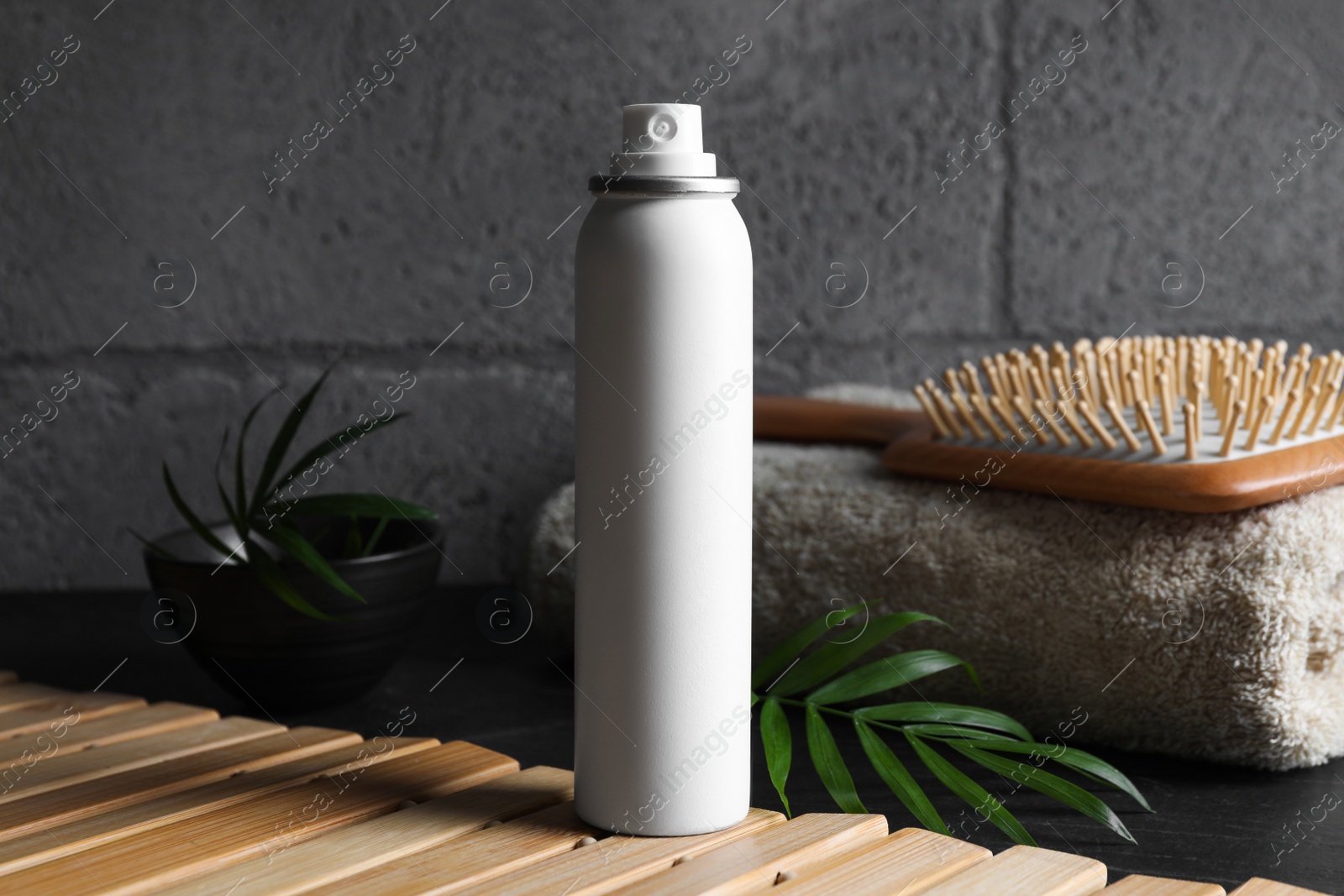 Photo of Dry shampoo spray, hairbrush and towel on wooden table near grey wall