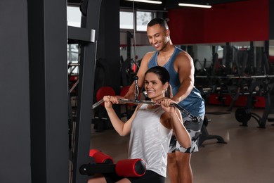 Photo of Happy trainer showing woman how to do exercise properly in modern gym