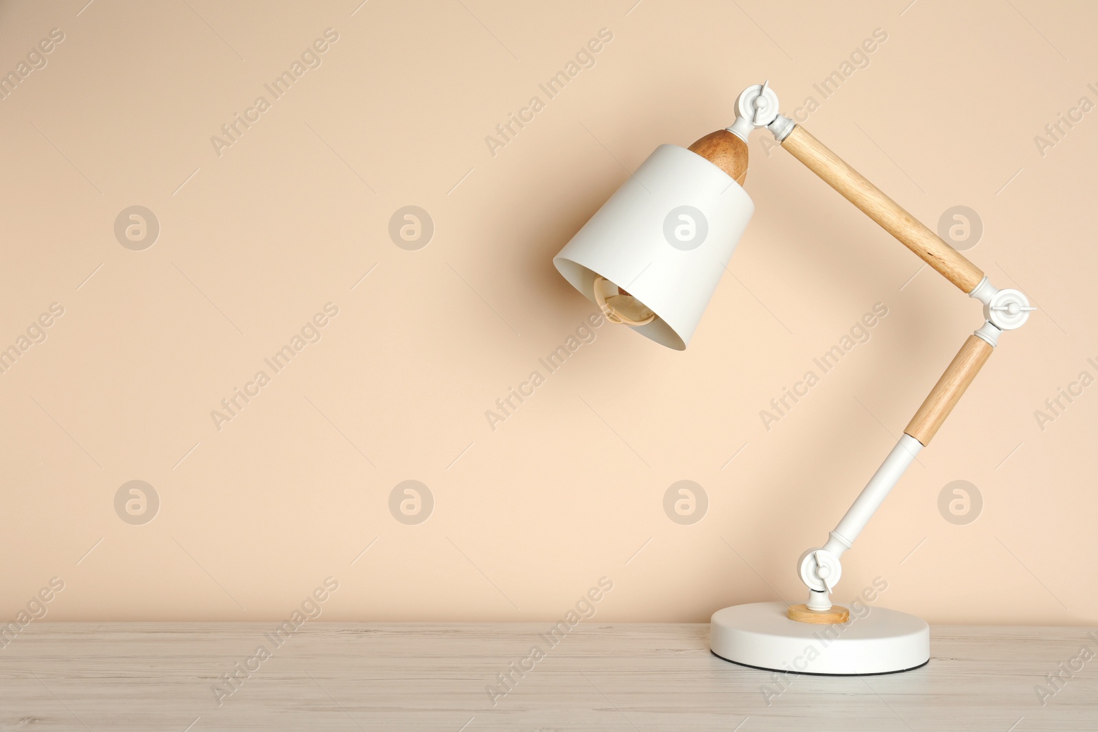 Photo of Stylish modern desk lamp on white wooden table near beige wall, space for text