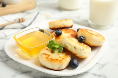 Photo of Delicious cottage cheese pancakes with blueberries, mint and honey on white marble table