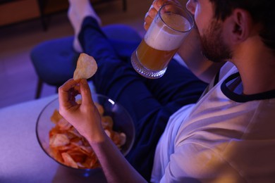 Photo of Man eating chips and drinking beer while watching TV on sofa at night, closeup. Bad habit