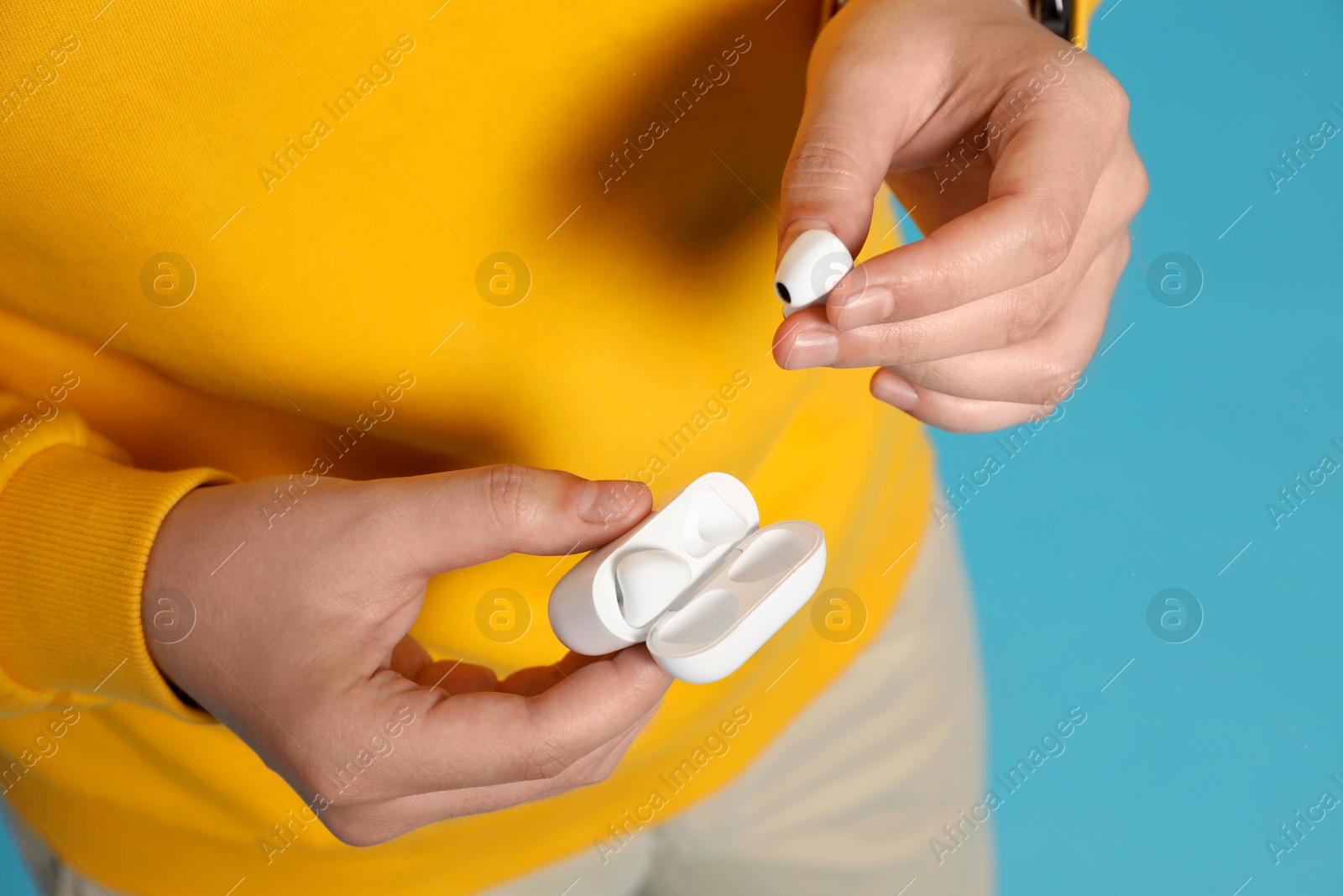 Photo of Man taking out earphones from case on light blue background, closeup