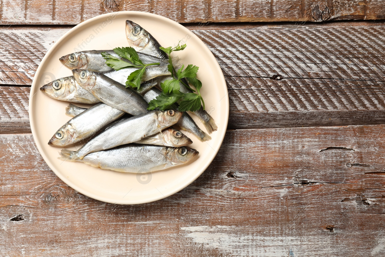 Photo of Fresh raw sprats and parsley on wooden table, top view. Space for text