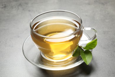 Photo of Cup of green tea and leaves on grey table