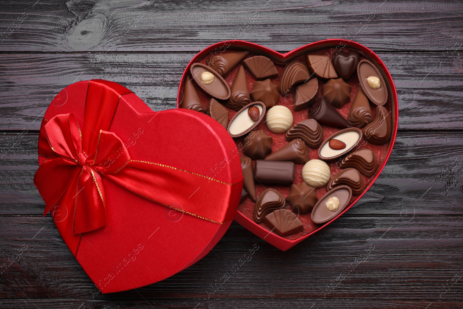 Photo of Heart shaped box with delicious chocolate candies on wooden table, top view