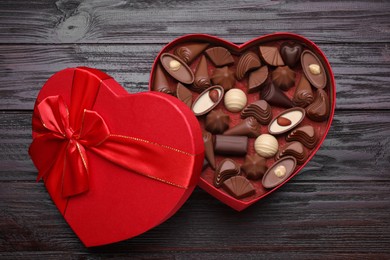 Photo of Heart shaped box with delicious chocolate candies on wooden table, top view