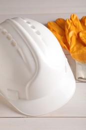 Hard hat and gloves on white wooden table, closeup. Safety equipment