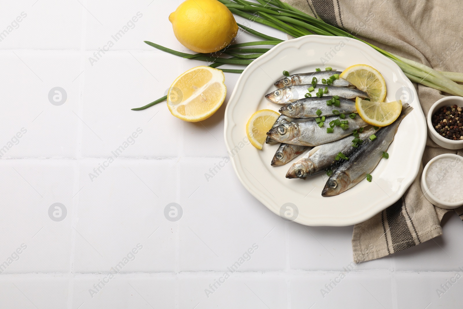 Photo of Fresh raw sprats, onion, spices and cut lemon on white tiled table, flat lay. Space for text