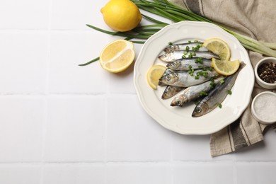 Fresh raw sprats, onion, spices and cut lemon on white tiled table, flat lay. Space for text