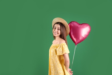 Portrait of young woman with heart shaped balloon on color background. Space for text